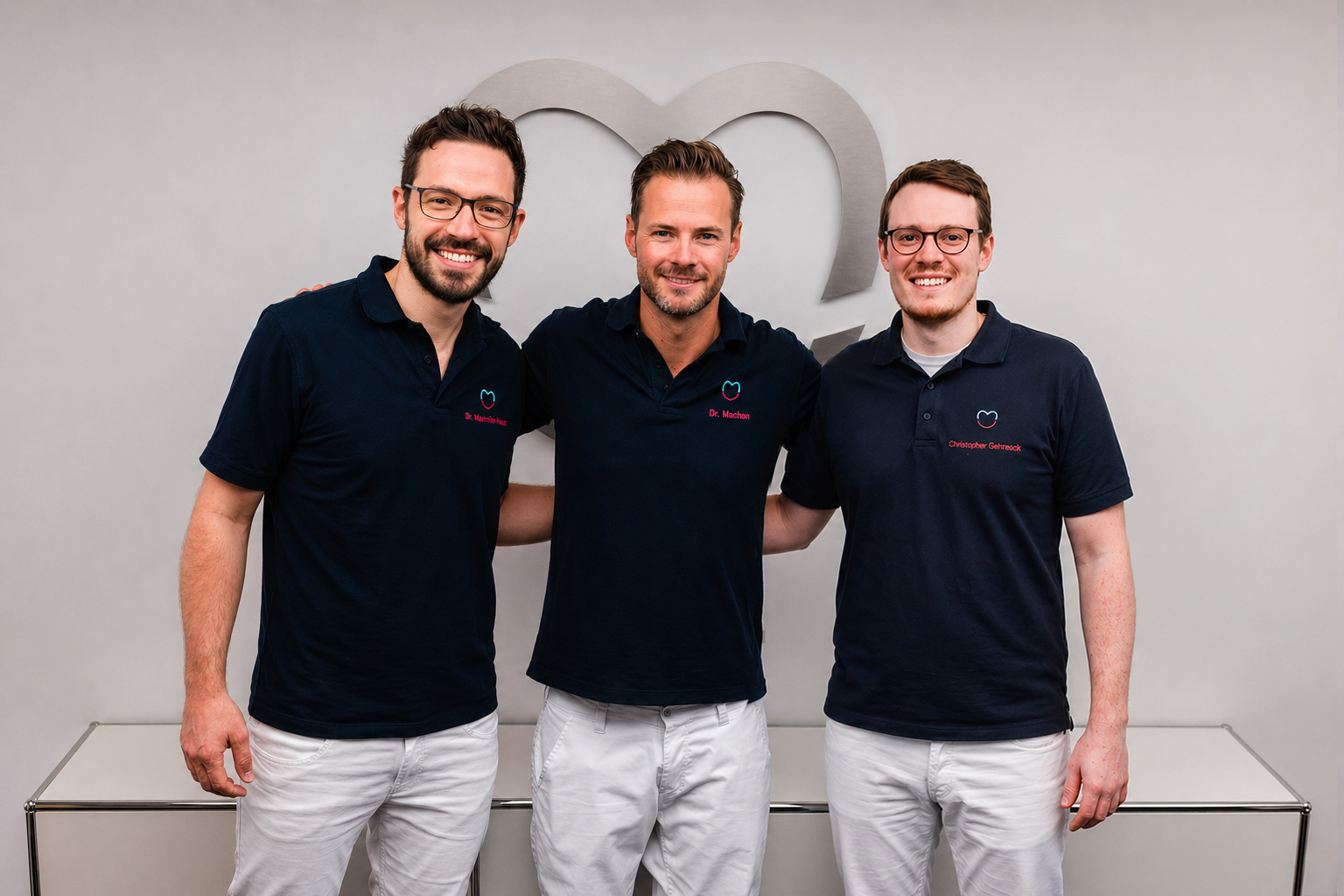 Die Zahnärzte Dr. Sebastian Machon, Dr. Fabian Seiz und Dr. Peter Michelbach vor dem Herz-Logo der Praxis